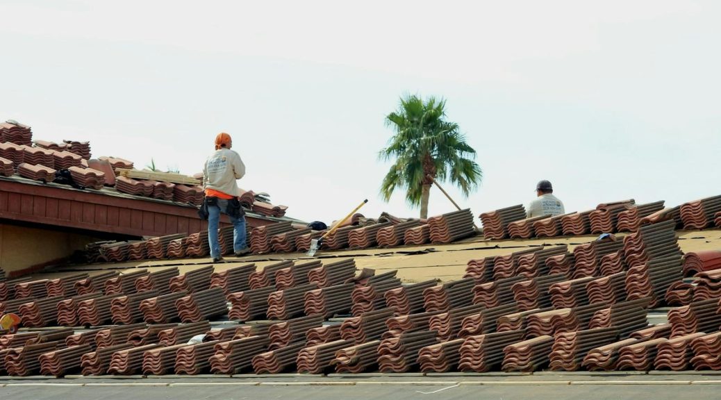 Construction workers installing terra cotta roof tiles under the sunny Phoenix sky.